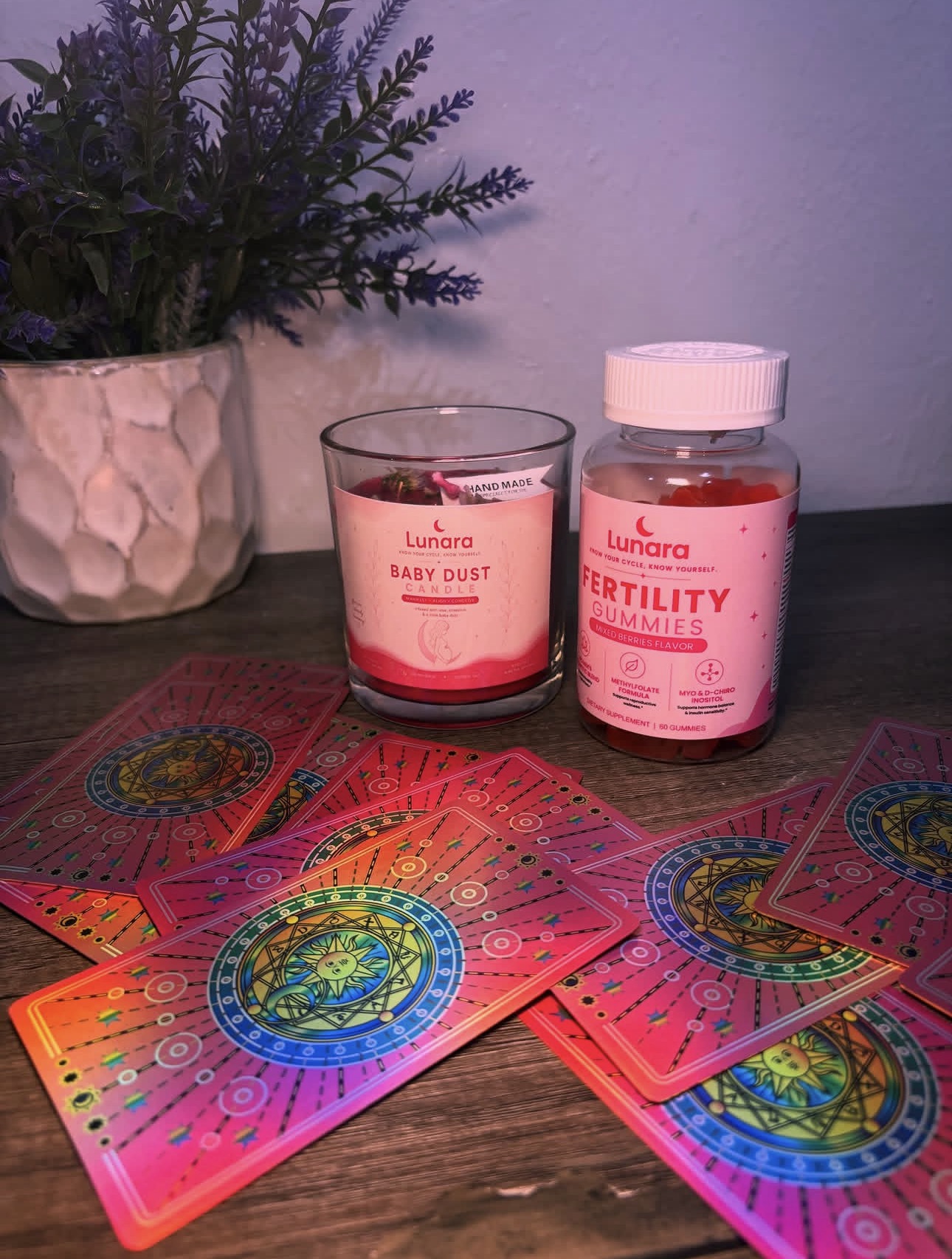 Lunara Baby Dust Candle, Fertility Gummies and affirmation cards on a wooden table