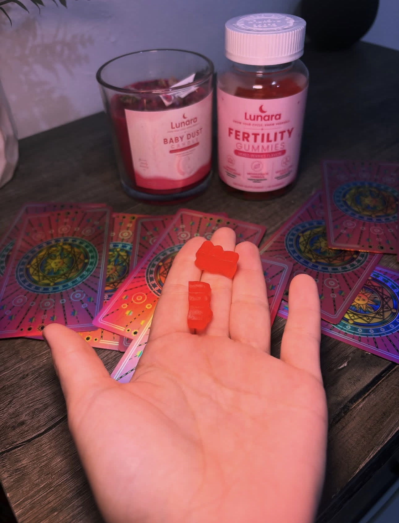 Two Lunara Fertility Gummies in hand, with the gummies jar and candle behind them